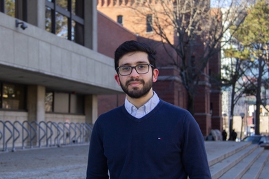 Photo of Meshkat Botshekan standing outdoors with an MIT building and a couple of trees in the background