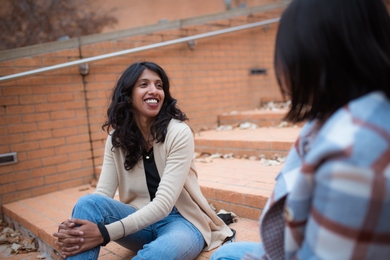 Photo of Athulya Aravind sitting on some steps and smiling while conversing with an unidentified companion
