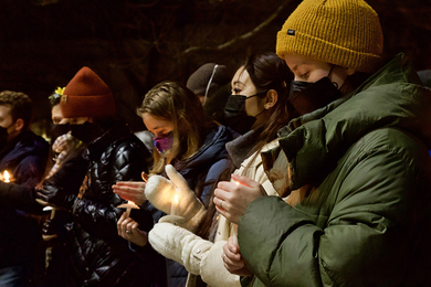 Students wearing face masks hold candles at a candlelight rally.