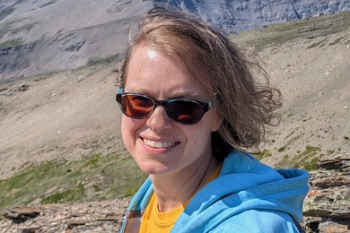 Headshot of Thea Keith-Lucas as she stands next to a mountain ridge
