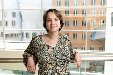 Portrait headshot of Fernanda de la Torre, who stands in front of a wall of windows. Behind her is the half brick, half steel MIT Stata Center.