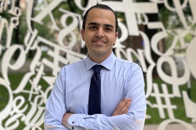 Portrait photo of Mohammad Khojasteh, standing inside a sculpture that surrounds him with white numbers and mathematical symbols