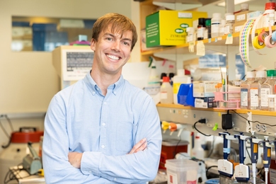 Mitch Murdock poses for a photo in a lab that's filled with pipettes, bottles, and other science equipment