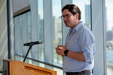 Photo of Giovanni Traverso speaking at a podium before a wall of glass windows