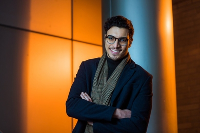 Assil Halimi stands against a backlit orange background.