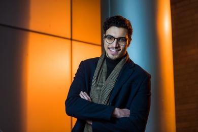 feature article about covid 19 pandemic Assil Halimi stands against a backlit orange background.