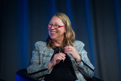 Antje Danielson looks to her right while sitting in front of blue curtains.