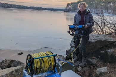 Sylas Horowitz stands by the edge of a lake holding their remotely operated vehicle.