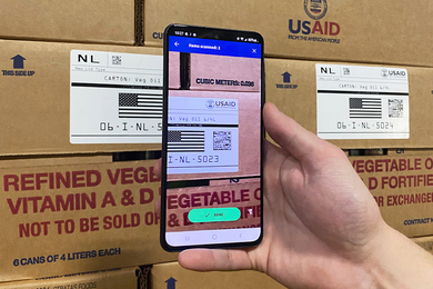 Closeup of a hand holding a smartphone, scanning a barcode on a carton of vegetable oil.