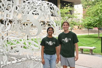 Anushree Chaudhuri and Cameron Dougal pose side-by-side, wearing green UA T-shirts
