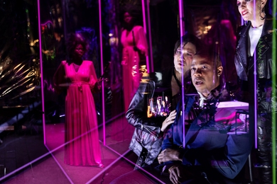 Actors in purple and pink light on a theater set with mirrored walls