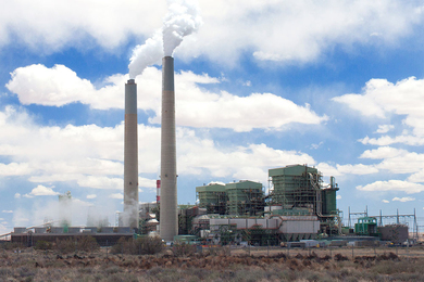 Photo of a power plant with two smokestacks in a desert area on a partly cloudy day