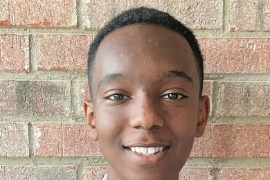 Portrait photo of Thomas Esayas, standing against a brick wall