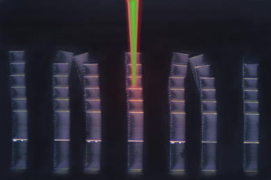 Seven tall, rectangular columns stand against a black background. The columns are made of a lattice-like pattern and some of them tilt at the top. In the center of the image, a green beam of light reaches between the top of the image and the middle column.