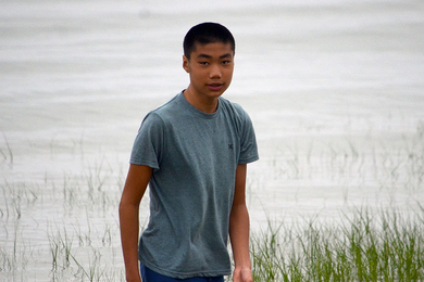 Teenager Dustin Liang standing in front of a lake with some tall grass in the foreground