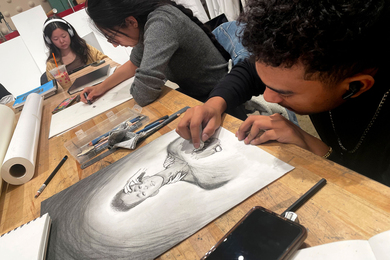 Charles Williams draws in an art class, with two students in the background.