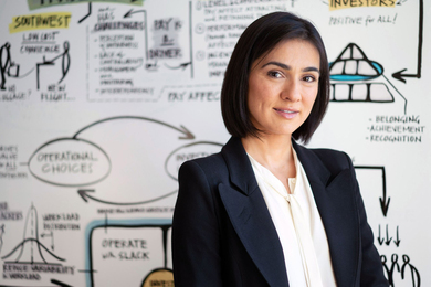 Zeynep Ton stands in front of a white board filled with illustrated notes and business ideas.