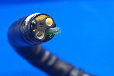 Closeup of the end of an endoscope shows sensors and 3 nozzles, one filled with neon-green material.
