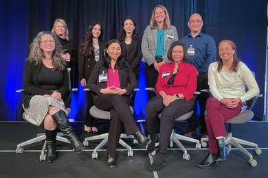 ride sharing research paper A group photo of eight women and one man in two rows, with back row standing and front seated, on a platform with dark curtains behind them.