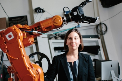 Julie Shah poses next to a large orange robotic arm