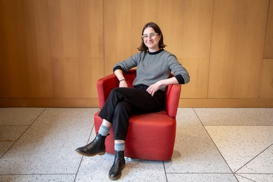 Anna Russo sits in a red armchair with her legs crossed, smiling at the camera