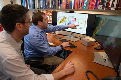 Two researchers sit at a desk looking at computer screens showing tornado radar images