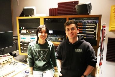 Maggie Lin and James Rock pose in front of a bank of radio equipment.