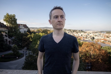Jonathan Ragan-Kelley stands outdoors in Budapest, with the city as a backdrop