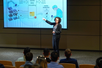 Laurence Willemet stands on stage and gestures toward her research poster.