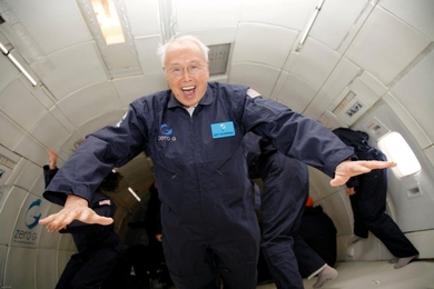An elderly Francis Fan Lee wears a blue jumpsuit and an expression of pure joy while floating mid-air on a reduced-gravity aircraft.
