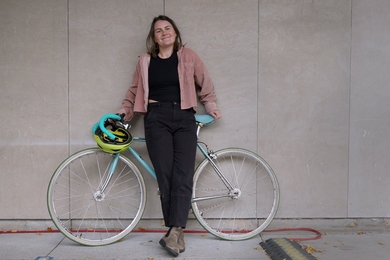 Bianca Champenois poses against a concrete wall with her bicycle 