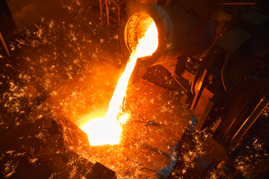 Glowing molten metal is poured in a dark factory, with lots of orange sparks.