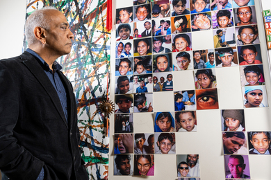 Pawan Sinha looks at a wall of about 50 square photos. The photos are pictures of children with vision loss who have been helped by Project Prakash.