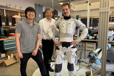 Sang-Yoep Lee, Harry Asada, and Erik Ballesteros stand in a lab. Erik is wearing the inside part of the new robotic suit, which resembles sports padding.