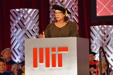 Diane Hoskins speaks on an indoor stage, at a lectern bearing MIT’s logo