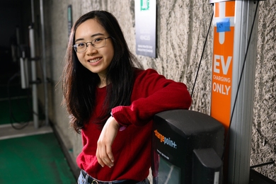 Elaine Liu leans against an electric vehicle charger inside a parking garage.