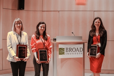 Betar Gallant, Frederike Petzschner, and Anne Carpenter stand next to a Broad Institute lectern holding award plaques.