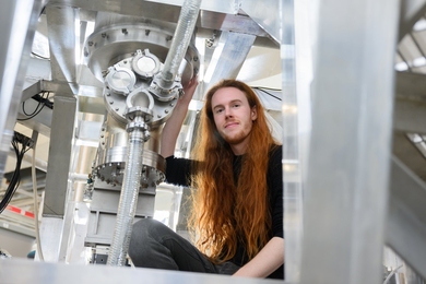 Thomas Varnish poses in the middle of PUFFIN, a large, stainless steel experimental facility.