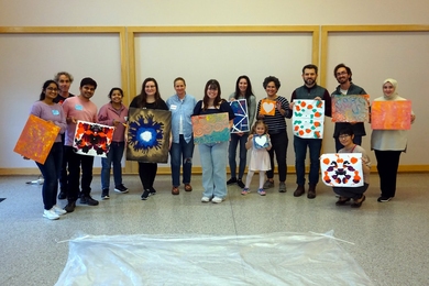 14 smiling volunteers and one child stand side by side, each holding a piece of colorful artwork.