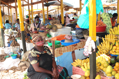 Woman with a patterned cloth face mask sits at a market stall in Kampala, Uganda. Most other people in the market are also wearing masks