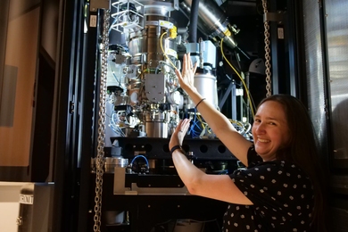 Sarah Sterling, smiling, next to barrel-shaped microscopy equipment