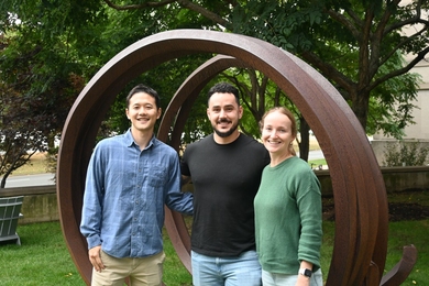 homas Lee, Laurențiu Anton, and Rosie Keller pose together in front of a large curved sculpture