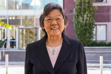 Jane-Jane Chen poses in front of a brick and glass building