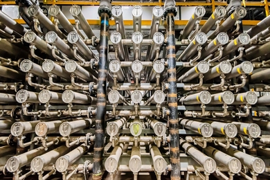 A rack of interconnected large silver tubes and pipes used to house filtration membranes for industrial chemical processing.