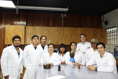 Nine people around a table in a lab, wearing lab coats and smiling