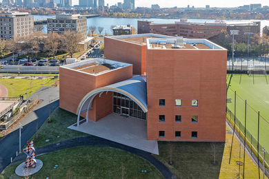 Aerial photo of the brick Edward and Joyce Linde Music Building with three distinct sections connected by a large atrium. The Charles River is in the background.