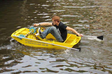 A person rides a DIY plastic boat that says “designed and built within 72 hrs in the ICC Fab Lab in Elyria, Ohio.”