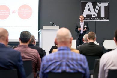 Bryan Reimer speaks on stage, standing next to a lectern