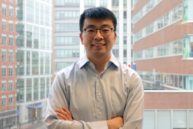 Haoran Li stands in front of a large window, with city buildings visible in the background