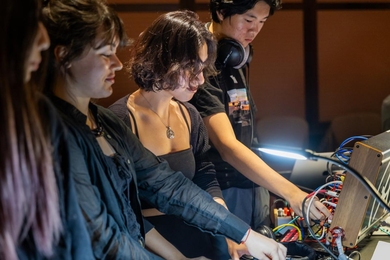Several students engage with a music panel that has many wires coming out of it. 